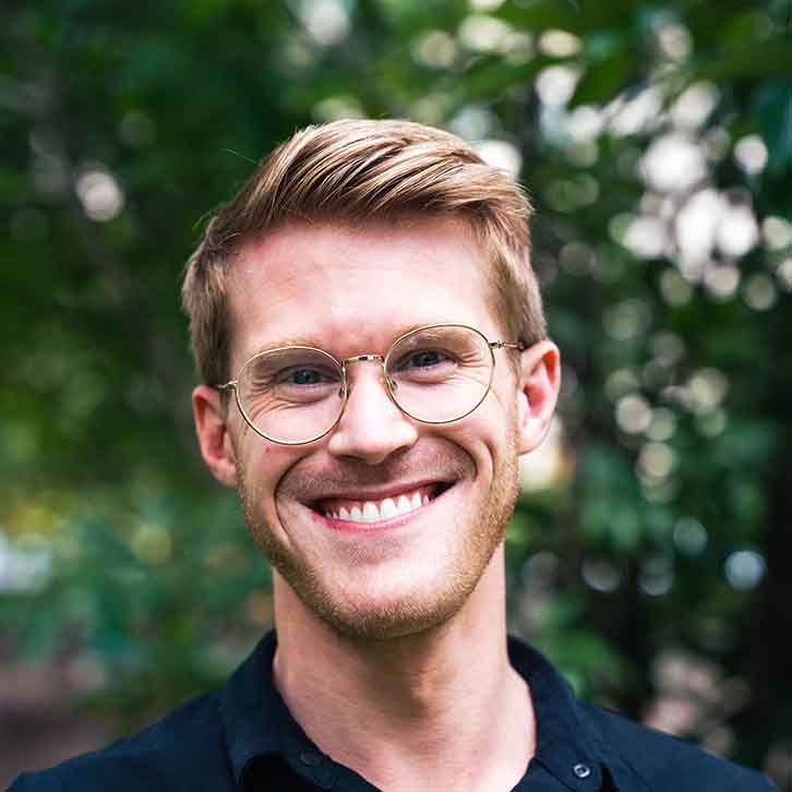 Smiling student in front of greenery.