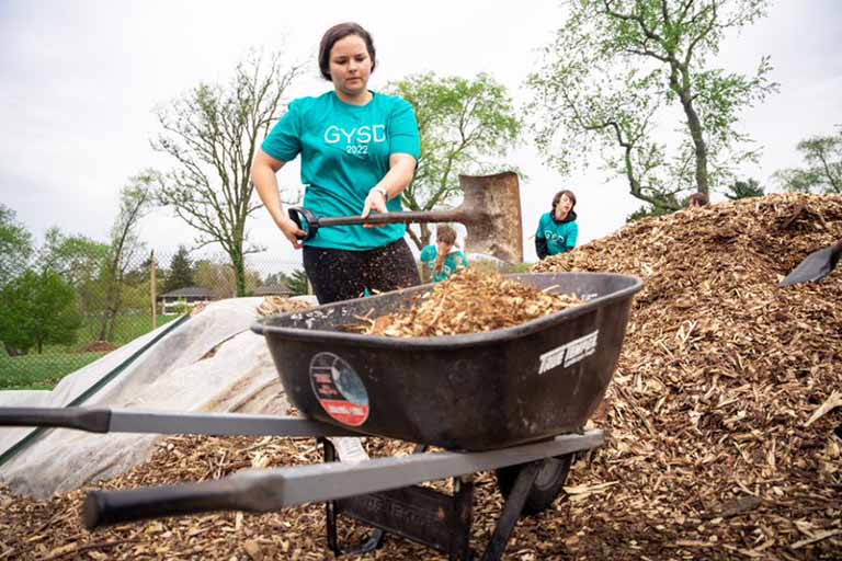 Woman shovels mulch into a wheelbarrow