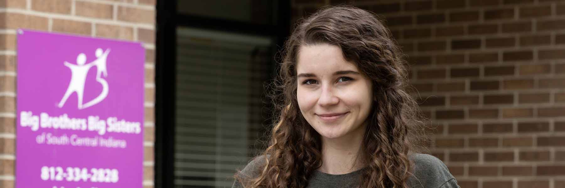 Student smiles in front of building.